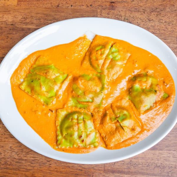 Green ravioli pasta in a creamy orange sauce, served on a white oval plate on a wooden table.