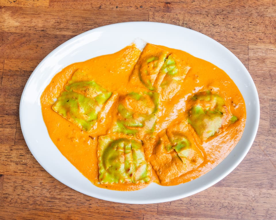 Green ravioli pasta in a creamy orange sauce, served on a white oval plate on a wooden table.