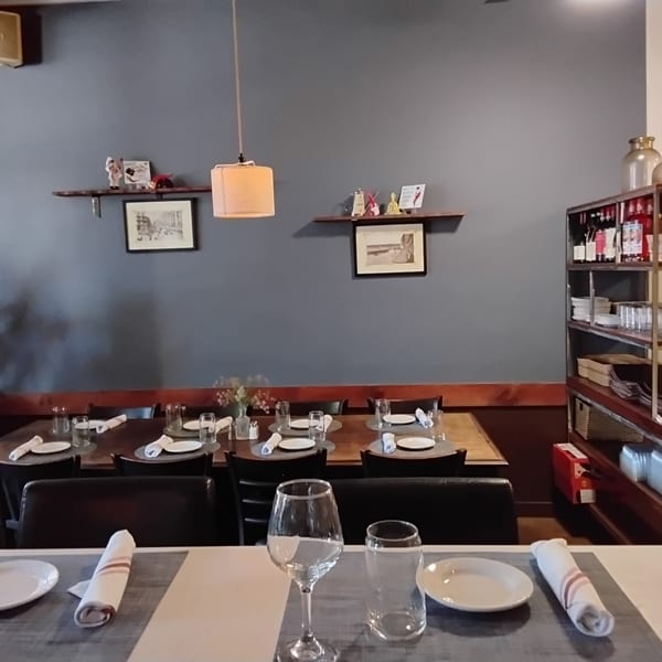 A restaurant dining room with set tables, a dark gray wall, and a shelving unit with bottles.