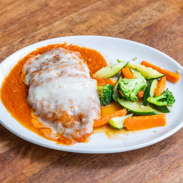 Chicken parmesan with melted cheese and red sauce, served with steamed broccoli, carrots, and zucchini.