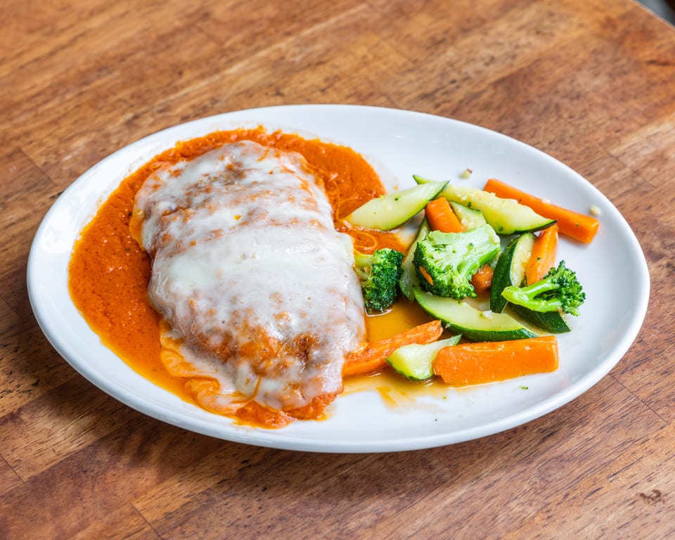 Chicken parmesan with melted cheese and red sauce, served with steamed broccoli, carrots, and zucchini.