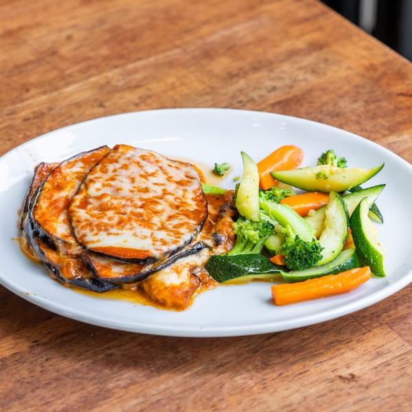 Eggplant parmesan with melted cheese and tomato sauce, served with steamed carrots, zucchini, and broccoli.