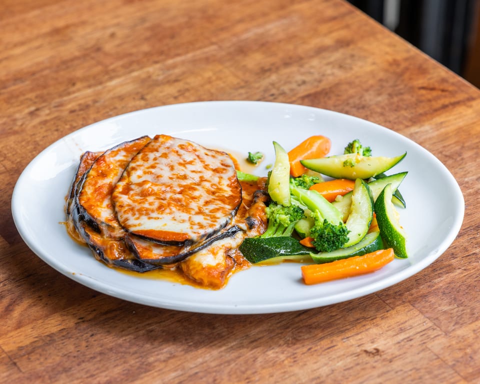 Eggplant parmesan with melted cheese and tomato sauce, served with steamed carrots, zucchini, and broccoli.