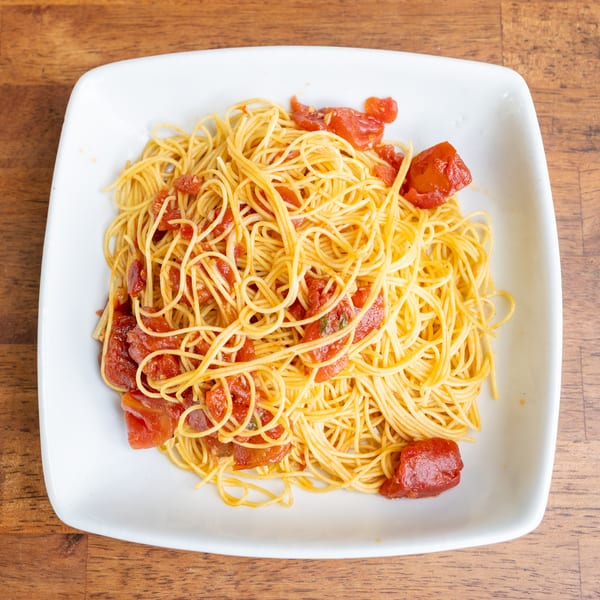 A white square plate filled with spaghetti and chunky tomato sauce on a wooden table.