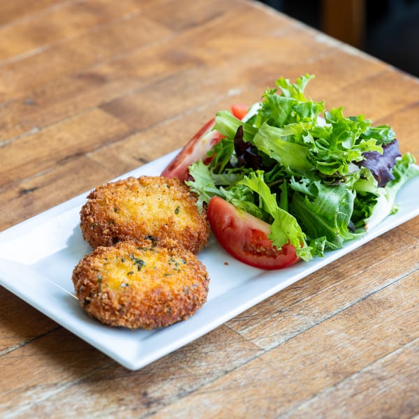 Two golden-brown crab cakes with a side salad of mixed greens and tomato wedges on a white plate.