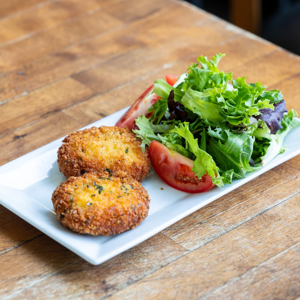 Two golden-brown crab cakes with a side salad of mixed greens and tomato wedges on a white plate.