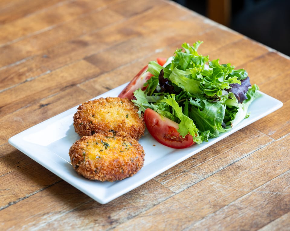 Two golden-brown crab cakes with a side salad of mixed greens and tomato wedges on a white plate.