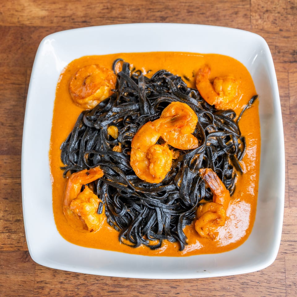 Black squid ink pasta with shrimp in a vibrant orange sauce, served on a white plate.