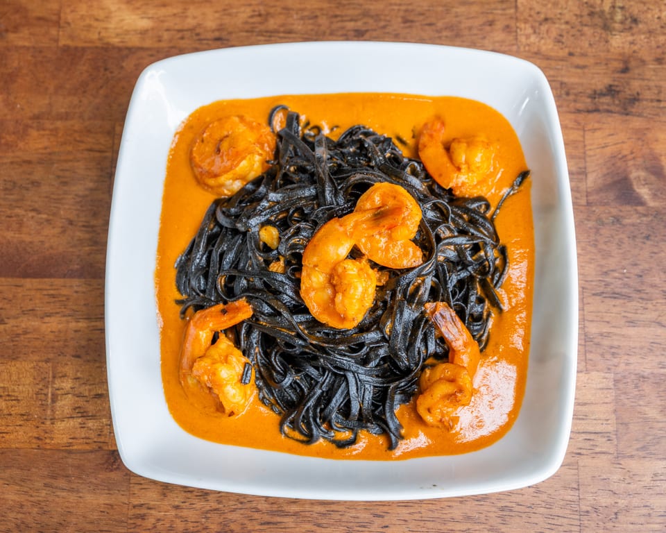 Black squid ink pasta with shrimp in a vibrant orange sauce, served on a white plate.