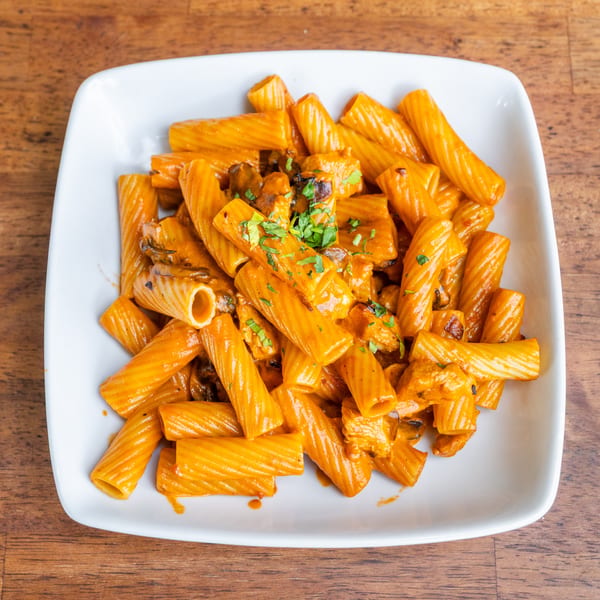 Rigatoni pasta with creamy orange sauce, chicken, mushrooms, and parsley in a white bowl.