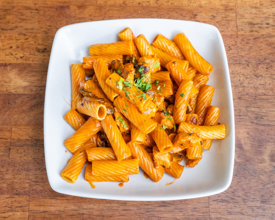Rigatoni pasta with creamy orange sauce, chicken, mushrooms, and parsley in a white bowl.