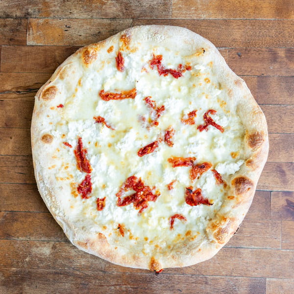 White pizza with ricotta cheese and sun-dried tomatoes on a wooden table.