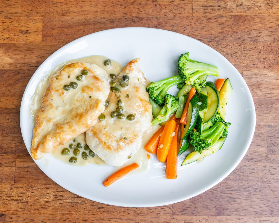 Chicken piccata with capers and creamy sauce, served with steamed broccoli, carrots, and zucchini.