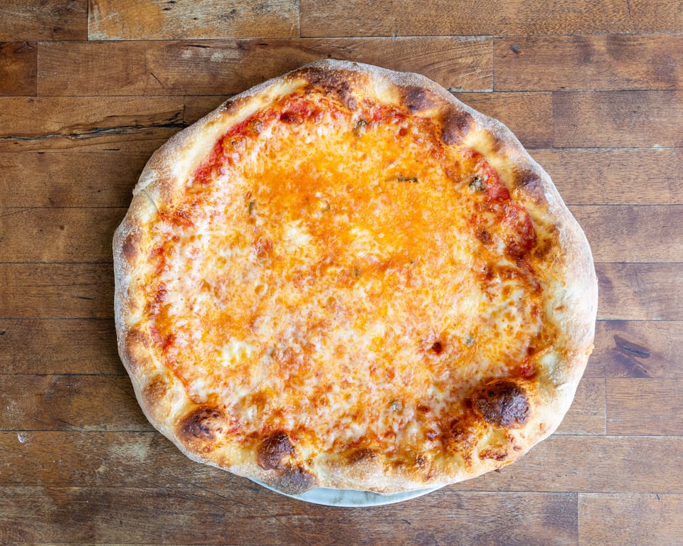 A whole cheese pizza with a golden crust sits on a rustic wooden table.