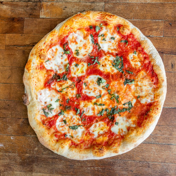A whole Margherita pizza with fresh mozzarella, tomato sauce, and basil on a wooden table.