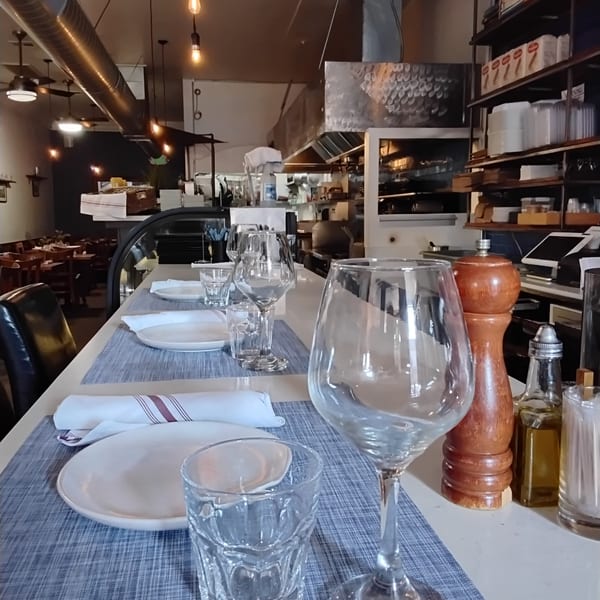 Restaurant interior with a bar counter set with plates and glasses, and a kitchen in the background.