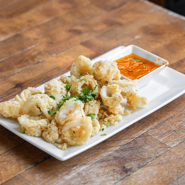 Crispy fried calamari with fresh parsley and a side of red dipping sauce on a white plate.