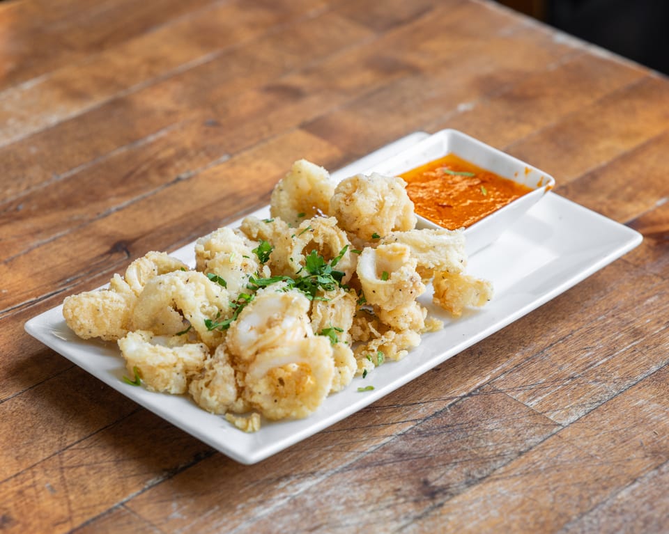 Crispy fried calamari with fresh parsley and a side of red dipping sauce on a white plate.