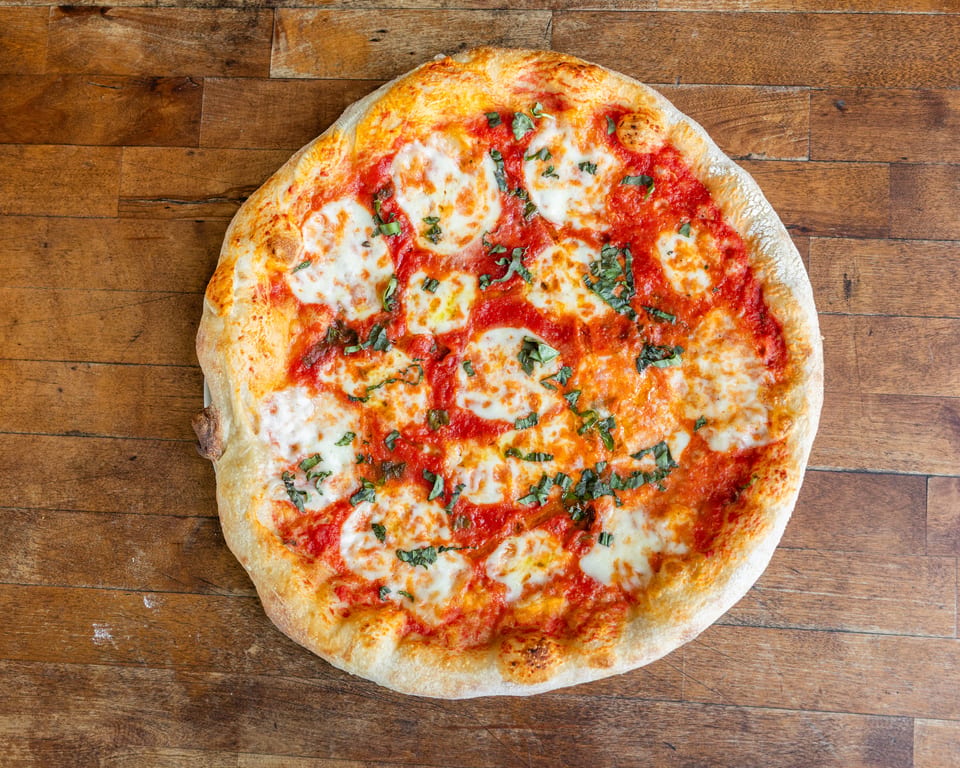 A whole margherita pizza with fresh basil, mozzarella, and tomato sauce on a wooden table.