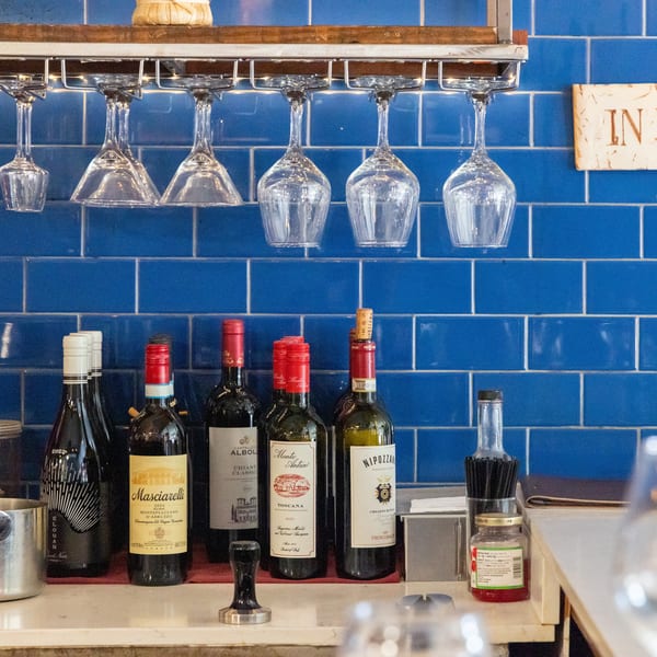 Wine bottles and inverted glasses sit on a bar counter against a blue tiled wall.