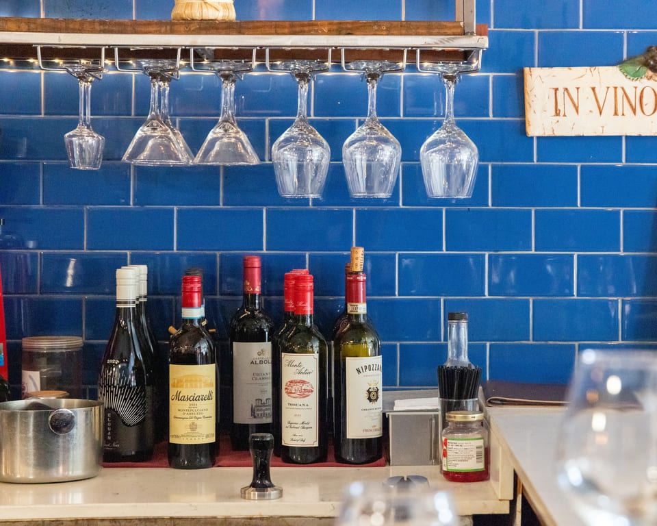 Wine bottles and inverted glasses sit on a bar counter against a blue tiled wall.
