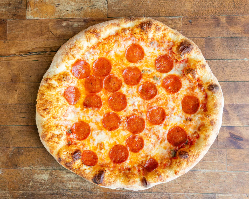 A whole pepperoni pizza with a golden crust and melted cheese on a rustic wooden table.
