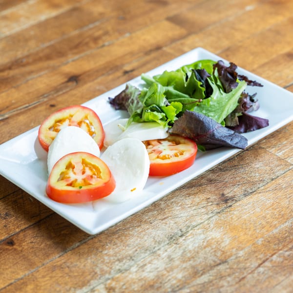 Caprese salad with sliced tomatoes, mozzarella, and mixed greens on a white rectangular plate.