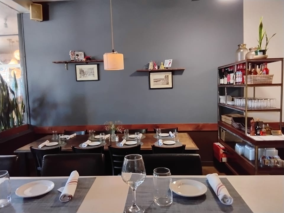 A restaurant dining room with set tables, dark gray walls, and a shelving unit with bottles.