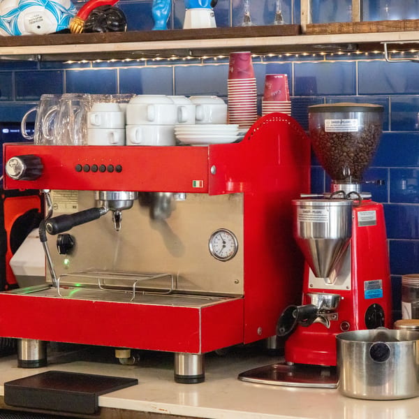 A red espresso machine and coffee grinder sit on a counter with blue tiled backsplash.