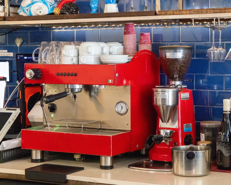 A red espresso machine and coffee grinder sit on a counter with blue tiled backsplash.