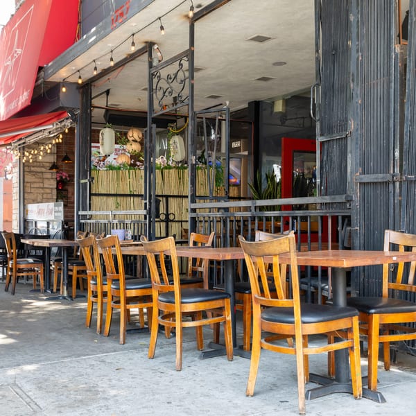 Empty outdoor patio seating with wooden tables and chairs in front of a restaurant.