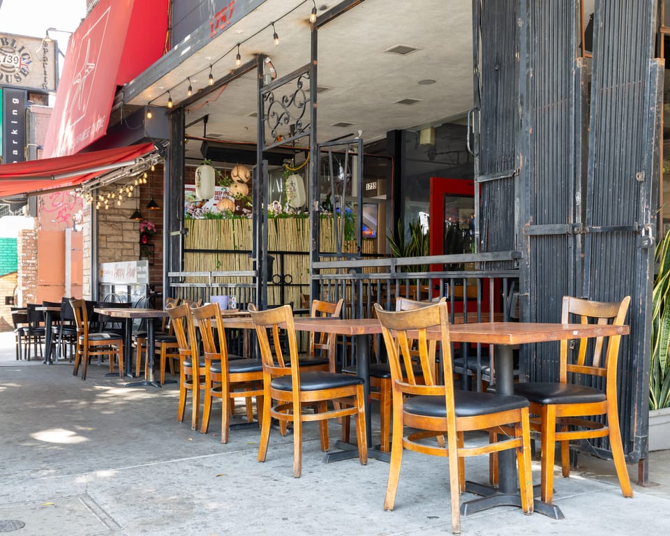 Empty outdoor patio seating with wooden tables and chairs in front of a restaurant.